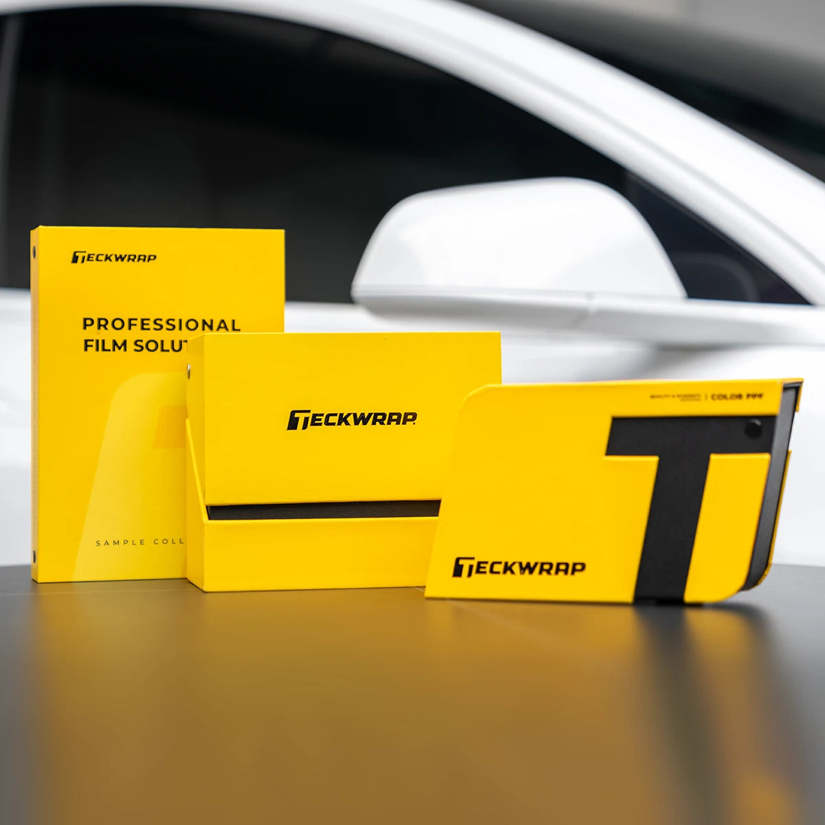 TeckWrap Swatches 2025 Set with yellow sample collection boxes displayed in front of a white car