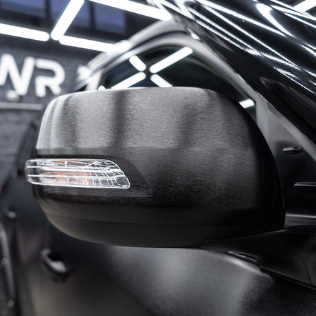 Detailed shot of a car side mirror wrapped in TeckWrap Brushed Black structured vinyl, emphasizing the elegant brushed metal texture.